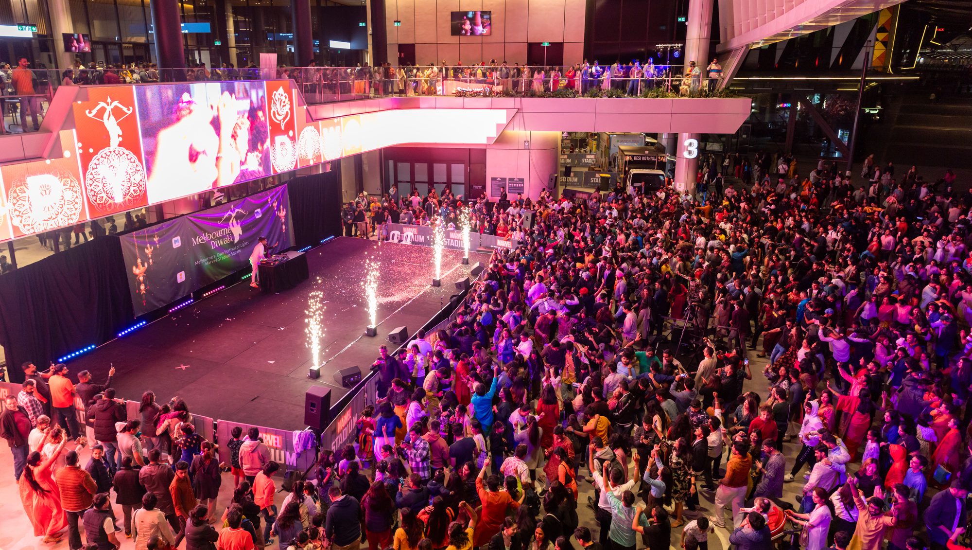 A packed crowd around the Melbourne Diwali stage at Marvel Stadium, with cold-spark fountains lit on stage